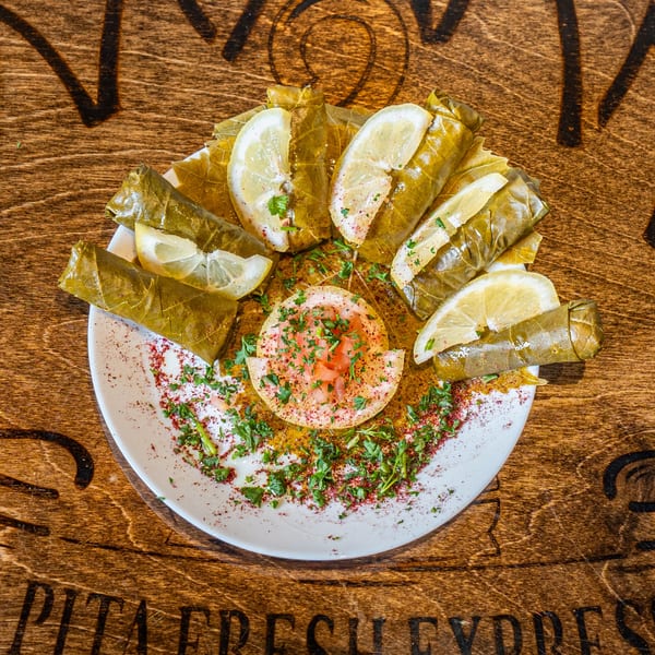 Pita Fresh Express's Mediterranean dolmades, garnished with lemon wedges, parsley, and spices on a white plate.