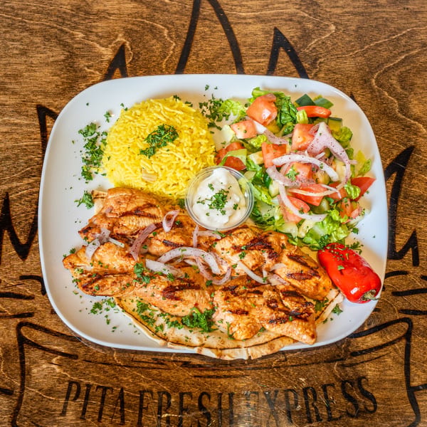 Mediterranean grilled chicken with yellow rice, fresh salad, and garlic sauce on a white plate.