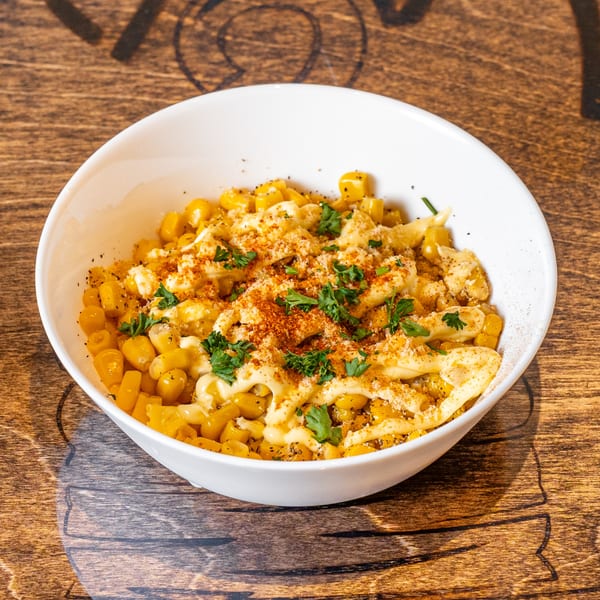 A white bowl filled with corn, drizzled with sauce, and garnished with paprika and parsley.