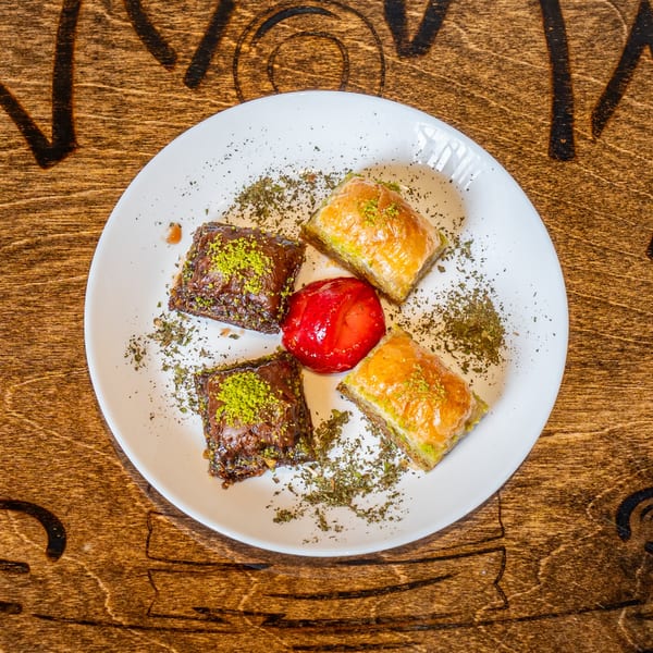A white plate of baklava, two chocolate and two pistachio, with a red candied fruit and herbs.
